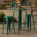 An emerald green metal bar table with two bar stools on an outdoor patio.