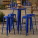 A Lancaster Table & Seating blue quartz bar table with 4 blue metal stools on an outdoor patio.