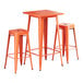 A Lancaster Table & Seating bar height outdoor table in amber orange metal with two backless barstools.