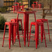 A Lancaster Table & Seating red metal bar table with four backless barstools on an outdoor patio.