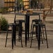 A Lancaster Table & Seating onyx black bar height outdoor table with four backless barstools on a patio.