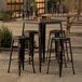 A Lancaster Table & Seating distressed copper bar height outdoor table with stools and glasses on top.