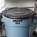 A man standing next to a large Rubbermaid trash can with a lid.