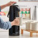 A person using a Choice black stainless steel airpot to pour coffee into a white mug.