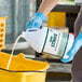 A person in blue gloves pouring Noble Eco Strike multi-purpose enzymatic cleaner into a bucket.
