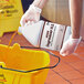 A person holding a white bottle of Noble Eco Degreaser pouring liquid into a yellow bucket.