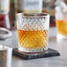 An Acopa Aurelius rocks glass of amber liquid on a stone coaster.