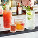 A bartender pouring different colored drinks into Acopa Zion shot glasses on a table in a cocktail bar.