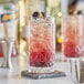 A close up of a Gardenia Beverage Glass filled with a blackberry and lemonade cocktail with a lemon wedge.