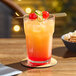 An Acopa Memphis beverage glass of orange and red drink with a cherry on top on a coaster.