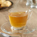 A glass cup of Bigelow green tea on a saucer with a spoon and cookies.