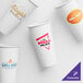 A group of customizable white paper hot cups with different designs including logos and red and orange text.