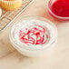 A bowl of white frosting with red swirls on top of a cupcake.