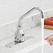 A hand using a Waterloo deck mount sensor faucet with a gooseneck spout over a sink.