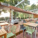 An Aura carbon stainless steel infrared patio heater on a wooden deck with tables and chairs.
