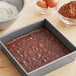 A brownie in a pan next to a bowl of Ghirardelli Dutch cocoa powder and eggs.