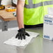 A person wearing black gloves cleaning a table with a white Lavex industrial wiper.