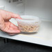 A hand holding a Pactiv translucent plastic container of food.
