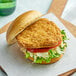 A chicken burger with lettuce, tomato, and cheese on a paper.