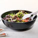 A black bowl of salad with a fork and spoon.