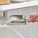A hand using a Choice stainless steel flour scoop to scoop flour into a silver container.