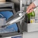 A hand using a Choice stainless steel scoop to scoop ice into a glass.