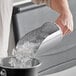 A person using a Choice stainless steel flour/breading scoop to add ice to a bucket.