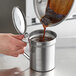 A person pouring brown liquid into a Choice stainless steel oil container.