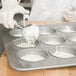 A person pouring white batter into a Chicago Metallic oversized muffin pan.