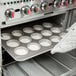 A person using a Chicago Metallic mini cake and oversized muffin pan to bake white muffins.