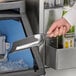 A person using a Choice stainless steel bar scoop to remove ice from a metal container.