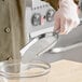 A person in a white coat using a Choice stainless steel bar scoop to pour white sugar into a bowl.