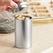 A hand holding a 2 9/16" x 4 5/16" silver tea tin.