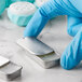 A person in blue gloves holding a silver metal tin with white substance and a slide top lid.