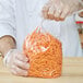 A person in gloves holding an LK Packaging plastic food bag of shredded carrots.