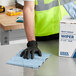 A person in a safety vest and black gloves cleaning a table with a blue Lavex industrial wiper.