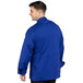 A man wearing an Uncommon Chef deep royal blue long sleeve chef coat with a mesh back.