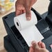 A hand holding a PointPlus thermal cash register paper roll.