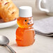 A clear plastic bear-shaped honey bottle with a white lid on a table with a spoon.