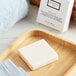 A Beekman 1802 Fresh Air bar soap in a white box on a wooden tray next to a towel.