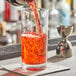 A bartender pouring red liquid from a silver shaker into an Acopa Straight Up cocktail glass.