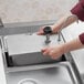 A person using a ServSense stainless steel pump dispenser to fill a metal container.