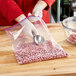 A person in red gloves using a Ziploc two gallon storage bag to put food in a glass bowl.