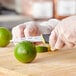 A hand in yellow gloves uses a Schraf serrated paring knife to cut a lime.