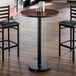 A round, 30-inch laminated table with a reversible cherry and black top, shown with a black pedestal base in a dining setting.