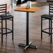 A square bar height table with a reversible walnut and oak laminated top and a black cast iron base.