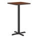 A square bar height table with a reversible walnut and oak laminated top and a black cast iron base.