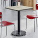 A square, reversible gray and white laminated table with a black cast iron pedestal base, shown in a dining area.