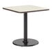 A square standard height table with a reversible white birch or ash laminated top and a black cast iron pedestal base.