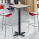 A square bar height table with a reversible gray and white laminated top and a black cast iron base.